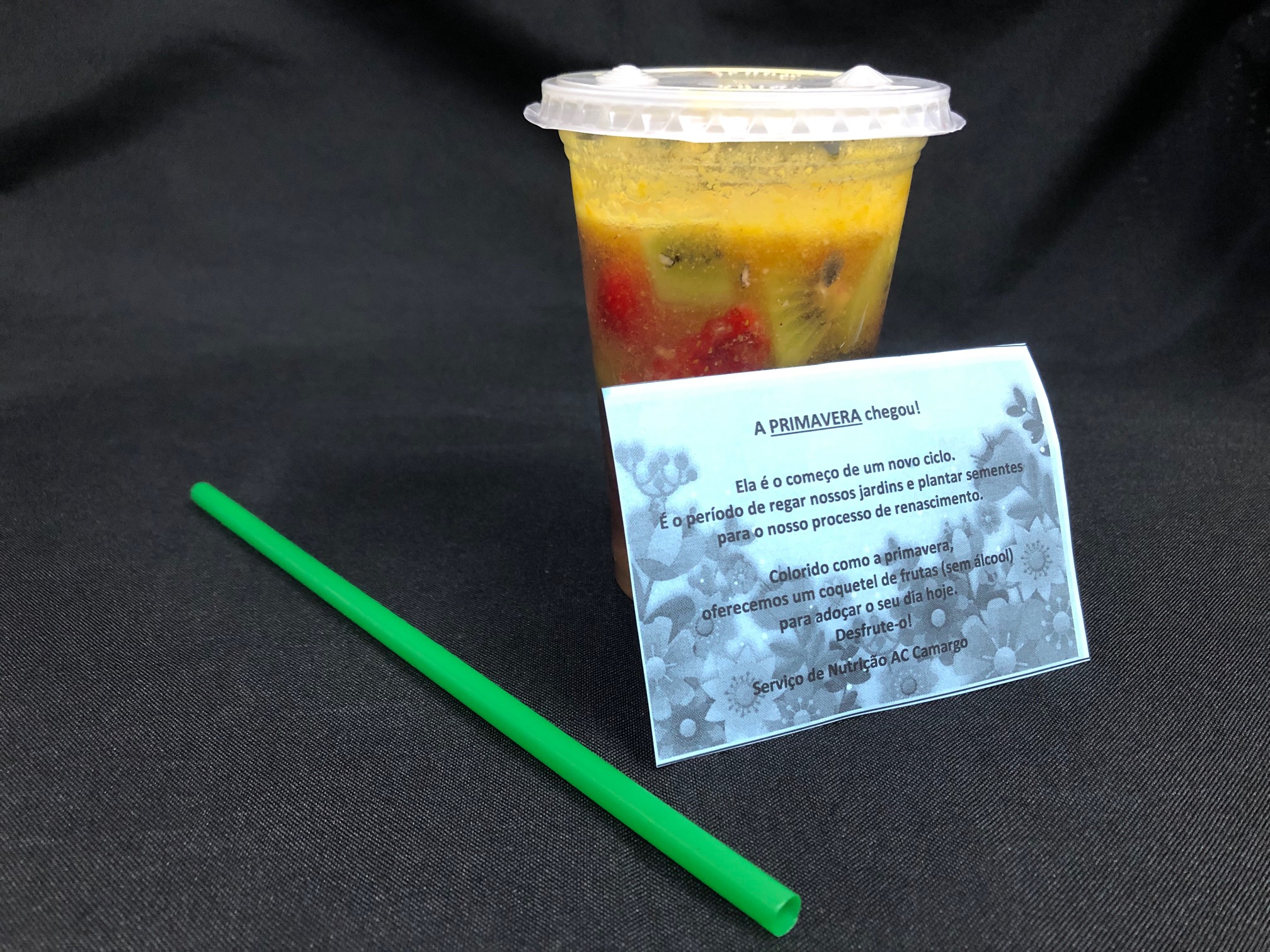 Copo de plástico transparente com um líquido amarelado, que é o coquetel de frutas