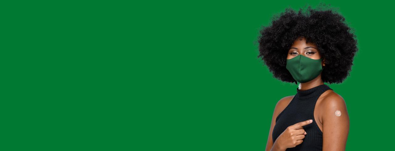 Mulher negra com máscara verde e braço vacinado, cabelo black power